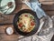 Omelet with tomatoes and spinach in a round cast iron pan on an old Board table, cotton napkins and coarse salt in a