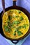 Omelette with broccoli, herbs and sesame seeds in frying pan.