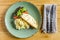 Omelette, tomatoes, herbs and bread on a green plate, cutlery, on a wooden table. View from above