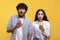 Omg. Shocked indian couple using smartphones and looking at camera with open mouth over yellow background, banner