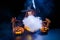 An ominous witch in a hat conjures over a jack-o-lantern. Traditional halloween characters. Mystical fog creeps over