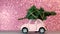 Omsk, Russia - Oktober 27, 2018: Toy model car with Christmas tree on on the roof rides on pink Blurred Glitter background.