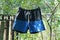 One blue black shorts hanging and drying on a wire with clothespins