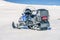 One blue snowmobile stands on a crust snow at slope in Norwegian mountains, back view. Warm day and very bright sun, no clouds,