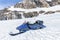 One blue snowmobile stands on snow close to stones in Norwegian mountains, warm day and bright sun, snow smelts, norwegian