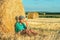 One boy sits at a haystack in a field on a sunny day and m thinks about something