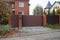 One brown iron gate and a fence of bricks and wooden boards