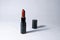 One Carrot-colored Lipstick and black caps stand vertically at a distance from each other on a white background