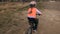 One caucasian children rides bike road track in dirt park. Girl riding black orange cycle in racetrack. Kid goes do