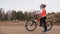 One caucasian children rides bike road track in dirt park. Girl riding black orange cycle in racetrack. Kid goes do