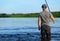 One Caucasian fisherman is standing in the water and holding the black fishing rod in his hand against the background of the