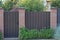 One closed iron brown door and part of a fence made of bricks and metal