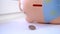 One coin will fall onto the table from a pink piggy bank
