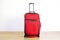 One colorful red textile suitcase on wheels with extended telescopic handle on wooden floor, white wall background. Baggage for tr