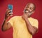One contemplative trendy mature african american man taking a selfie on a smart phone against a red studio background