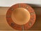 One deep orange plate with ethnic ornaments stands on a wooden table. View from above