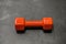 One dumbbell of orange color in the latex shell lies on the gray floor in the center of the photo