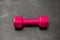 One dumbbell of pink color in the latex shell lies on the gray floor in the center of the photo