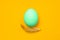 One egg colored in blue mint color and a feather on bottom on yellow background. easter background idea