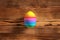 One egg is painted in 12 colors stripes, lying on a wooden table
