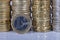 A one euro coin in front of many more coins stacked in columns o