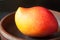 One fresh ripe mexican tropical mango fruit on dark background round homemade clay bowl.