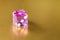 One glassy pink dice on a gold background in sunlight. The result is one. Selective focus macro photography