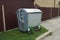 One gray large metal trash can stands outside in green grass