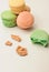 One green macaroon in the foreground lies a bite. Nearby are crumbs from a French pastry. In the background, three fresh colored