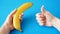 One hand tales banana, other hand make like on blue background