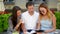 One Handsome Boy in White Shirt and Jeans Sitting near Two Beautiful Girls in Summer Dresses Studing Together Outdoors