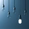 One hanging energy saving light bulb glowing different stand out from unlit incandescent bulbs