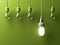 One hanging energy saving light bulb glowing different stand out from unlit incandescent lightbulbs