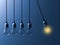 One hanging light bulb glowing different and stand out from unlit incandescent bulbs like newtons cradle on dark blue background