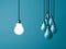 One hanging light bulb glowing and standing out from unlit bulbs on dark green pastel color background