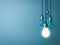 One hanging light bulb glowing with unlit incandescent bulbs on dark green pastel color background