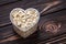 One heart of oat-flakes, uncooked oats on brown wooden board background. Laconic design. Symbol of love. Raw oatmeal, muesli. Diet