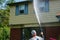One heavy overweight Caucasian man spraying water solution on the front of a house as part of his pressure washing service