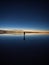 One isolated male tourist enjoying andes mountains sunrise mirror reflection on Salar de Uyuni salt flat lake in Bolivia