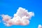 One isolated white cloud in a blue sky. Heaven background. Pink tint. Wallpaper. Beautiful cloudscape. Cumulus clouds. Weather