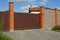 One large closed iron brown gate and brick wall fence