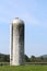 One large grey and white silo in a field of green grass