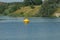 One large yellow plastic signal buoy in the blue water of the reservoir