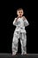 One little kid, boy, taekwondo athlete wearing white dobok isolated over dark background. Concept of sport, education