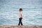 One lonely preschool pensive kid in white jersey and blue trousers walking upset along sea beach in spring