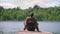 One man rests sitting on a pier on the shore of a lake in the woods. The tourist rests after a long walk, enjoys nature