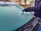 One man scrapes hoarfrost with plastic scraper from windshield of blue car. Male`s gloved hand in cold. Building is in distance.