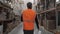 one man worker employee in orange vest walking along warehouse with boxes of products with camera movement