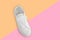One new white female or teen sneaker isolated on trend yellow-pink background. White textile sneaker with rubber soles with tied