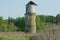 One old brown brick ruined water tower with a gray metal tank